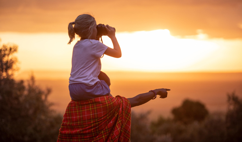 Child sits on the shoulders of a Maasai guide, over looking the Maasai Mara.