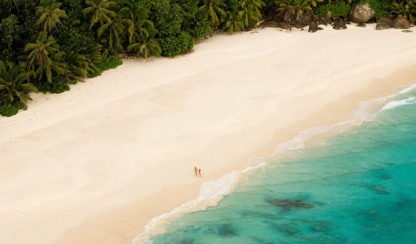 Couple walking on the beach of the private North Island in the Seychelles